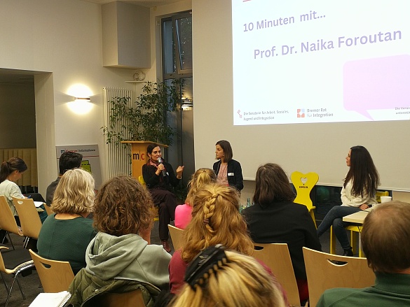 Prof. Dr. Naika Foroutan und Nadezhda Milanova sprechen auf dem Podium, im Vordergrund sitzen Teilnehmende
